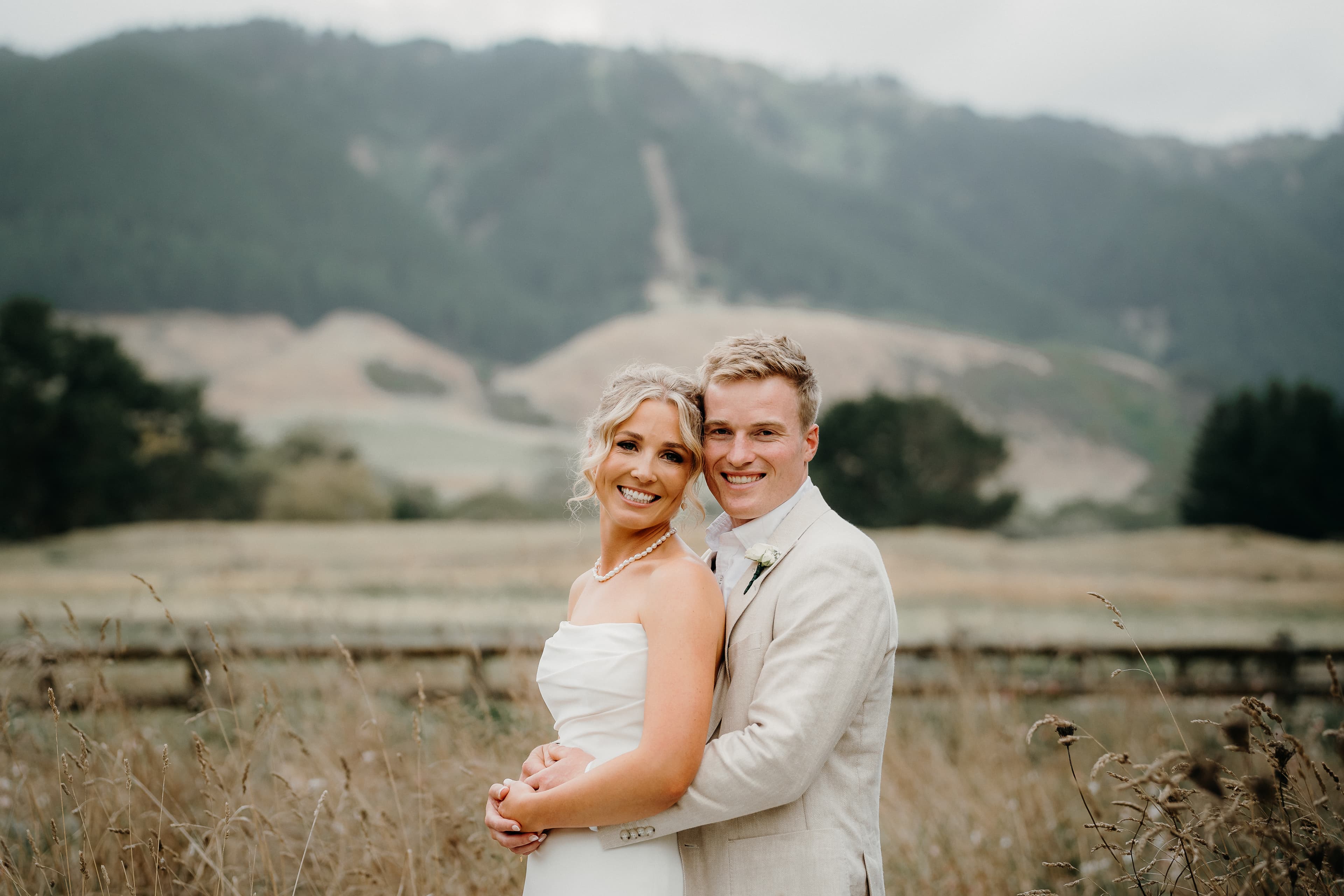 Bride and groom embracing in a golden field with misty mountains in the background